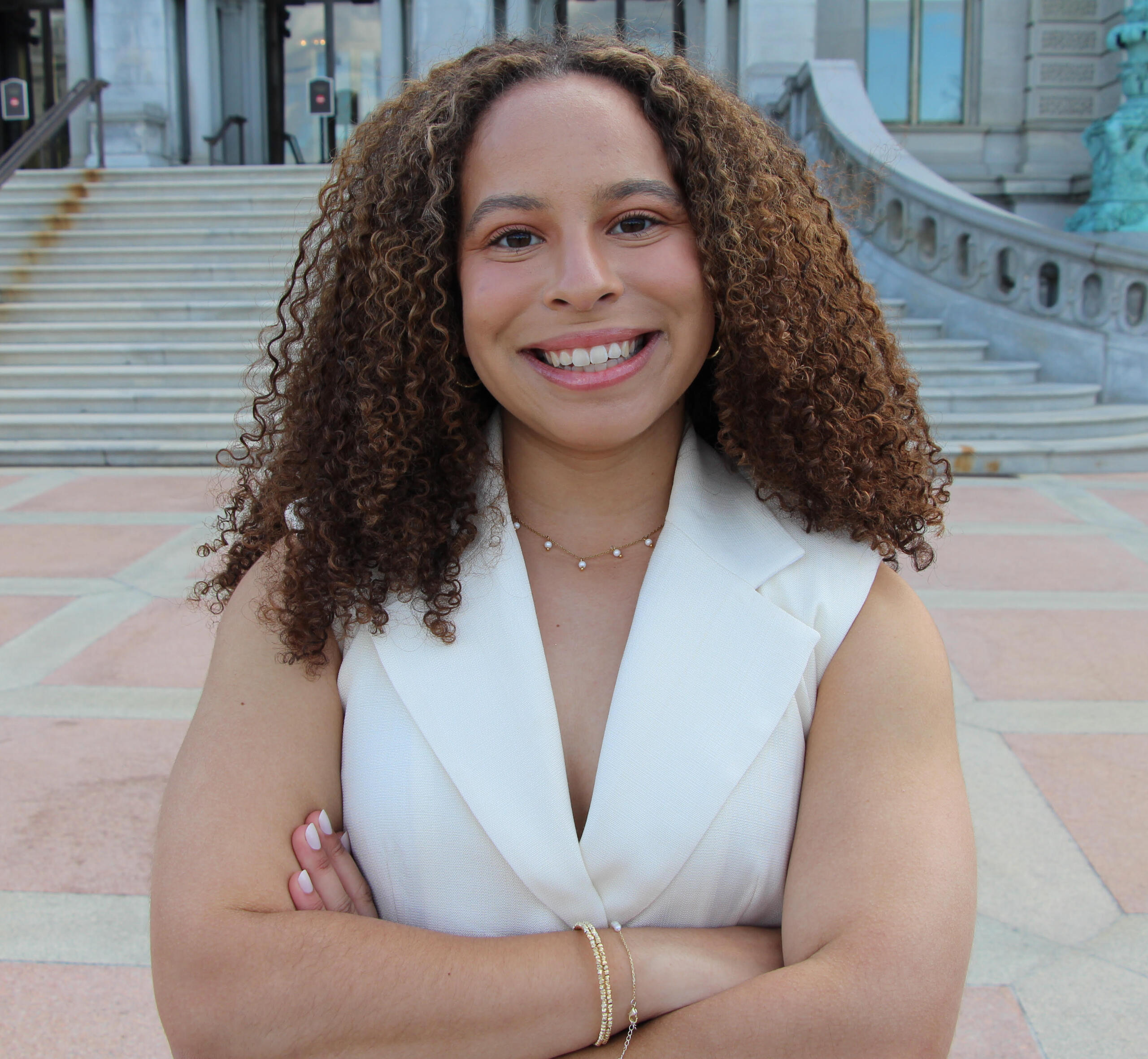 Avril Silva pictured in the White House Press Briefing room wearing a pink coat and black turtleneck.